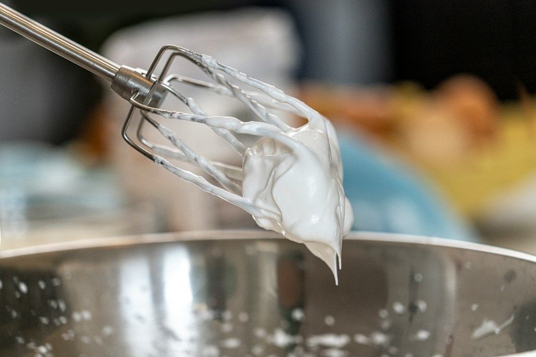 Visp med fluffig vit marängsmet över en rostfri bunke